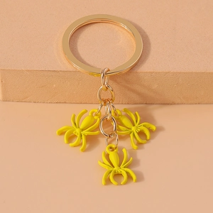 Macro detail of three bright yellow spider charms on a gold metallic keychain ring