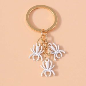 Detail of three white spider charms hanging from a polished gold keyring loop