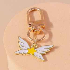 Détail d'un porte-clés doré avec des ailes en émail blanc et un motif d'étoile jaune vif