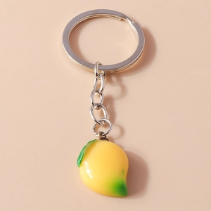 Detailed view of yellow mango keychain with green leaves on light pink backdrop