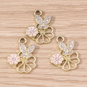 Pendentifs papillon doré avec émail rose et cristaux sur surface en bois clair