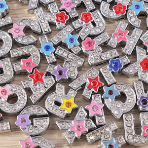 Primer plano de dijes de letras plateadas con pedrería y detalles de esmalte de colores