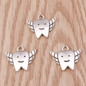 Vintage silver smiling tooth with wings charms for DIY jewelry making on wood background