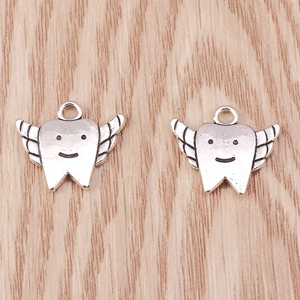Macro detail of two vintage silver wing-shaped tooth charms with smiling face on wood base