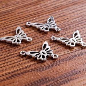 Silver hollow butterfly metal connectors for DIY jewelry making on dark wood table