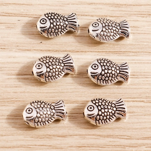 Macro detail of six retro silver fish charms for DIY jewelry making on wood