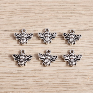 Detailed view of six vintage silver bee charms with hollow wings on a wood surface