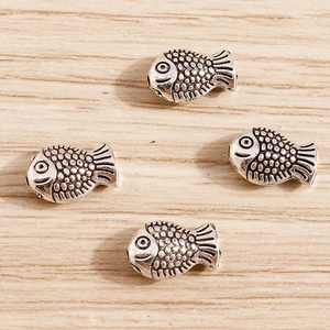 Close-up of four antique silver fish charms with detailed scales for DIY jewelry making