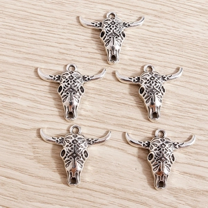 Five antique silver bull skull pendants with hollow carvings on light wood background