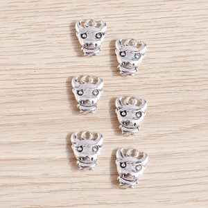 Detailed close-up of six vintage silver cow head charms on a light wood background