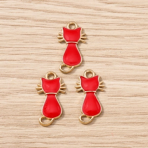 Détail de trois breloques chat en émail rouge avec crochets dorés sur fond de bois