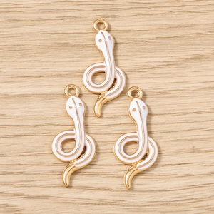 Detail of three golden snake pendants with white enamel for DIY jewelry making