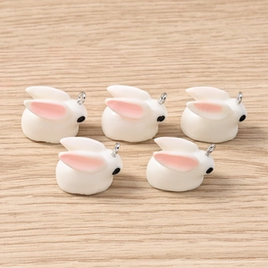 Detail of five white rabbit charms with pink ears and silver loops for DIY jewelry making