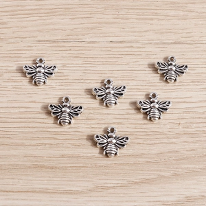 Detail view of six antique silver bee charms with hollow wings on wooden background