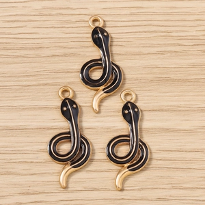 Detailed macro view of three gold-plated snake charms with black enamel on wood background