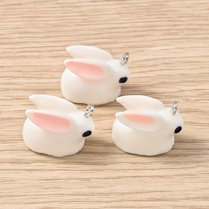 Three cute white resin bunny pendants with metal loops on a light wood background