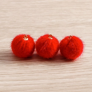 Set of three vibrant red pompom pendants with gold metal loops on light wood background