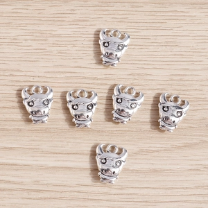 Set of 6 vintage silver alloy cow head pendants on light yellow wood grain background
