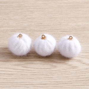 Three white plush pompom pendants with gold metal rings on a light wood surface