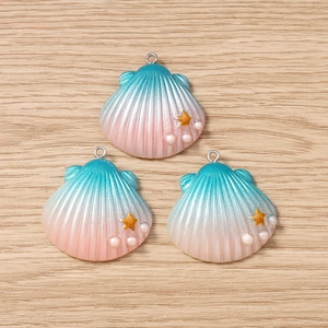 Three gradient shell charms with gold stars and pearls on a light wood background