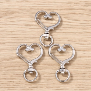 Tre fermagli a moschettone a forma di cuore d'argento con anelli rotanti su legno chiaro