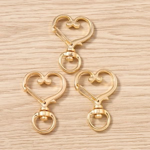 Tre chiusure a moschettone dorate a forma di cuore con anelli girevoli su fondo legno