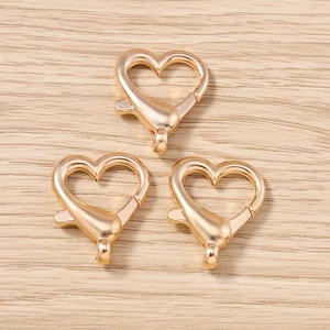 Dettaglio di moschettoni a forma di cuore dorati con meccanismo a molla su legno