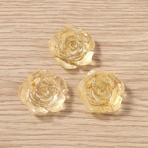 Tre ciondoli a rosa in resina trasparente con foglia d'oro su sfondo di legno