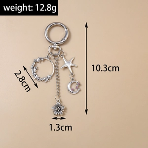 Détail du porte-clés argenté avec pendentifs étoile, lune et fleur sur fond beige