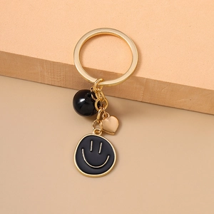Porte-clés tendance avec smiley doré, cœur et perle noire sur un fond texturé élégant