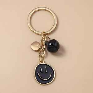 Porte-clés doré avec pendentif smiley noir, breloque coeur et clochette sur fond uni