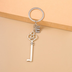 Silver alloy keychain with hollow key pendant and rhinestone letter E on pink background