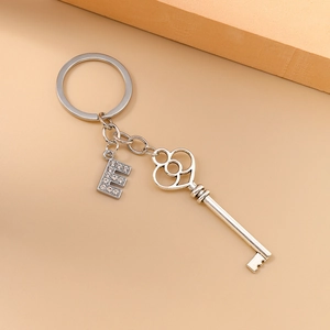 Close-up of silver key pendant and crystal-encrusted letter E on a metal keychain