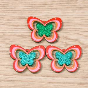 Three gradient butterfly acrylic charms with glitter detail on light wood background