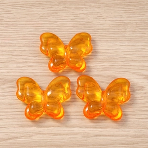Close-up of three translucent orange butterfly-shaped acrylic charms for DIY jewelry making