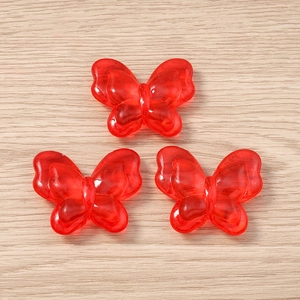 Three semi-transparent red acrylic butterfly pendants on a light wood background for DIY
