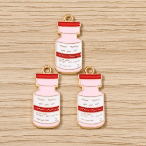 Vue détaillée de breloques en émail rose et blanc en forme de flacons médicaux dorés