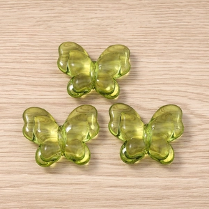 Three light green translucent butterfly charms for jewelry making on wooden background