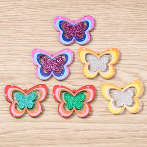 Macro detail of 3D layered butterfly charms with glitter finish on a wooden background