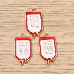Détail de trois pendentifs en émail en forme de poche de sang sur fond bois clair