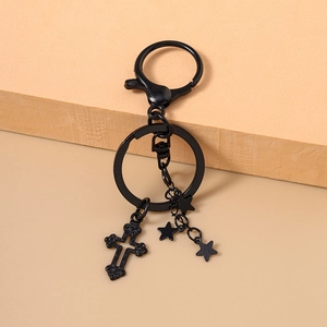 Detail eines gotischen schwarzen Metall-Kreuz-Schlüsselanhängers mit Sternen auf Beige
