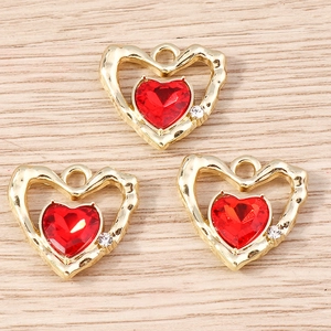 Vista macro di ciondoli a cuore dorati con cristallo rosso e strass per gioielli fai da te