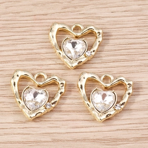 Dettaglio macro di tre ciondoli a cuore dorati con gemme su legno chiaro