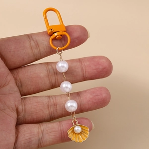 Marine style keychain with yellow scallop pendant and three white pearls on a lobster clasp