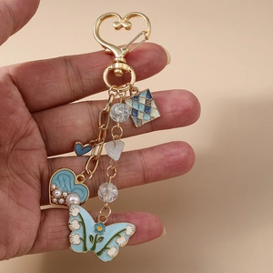 Fashionable butterfly keychain with blue heart and gold clip held in hand against beige background