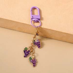 Detail view of purple grape keychain with matte carabiner on a beige textured stone base