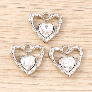 Vista macro di tre ciondoli a cuore Y2K in argento con zirconi su legno chiaro