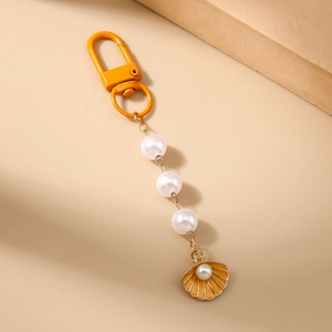 Detail of orange enamel shell keychain with pearls and lobster clasp on beige background