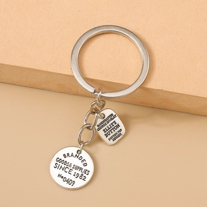 Détail d'un porte-clés vintage en métal argenté avec pendentifs gravés sur fond sable