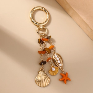 Détail d'un porte-clés doré sur le thème marin avec étoile de mer, coquillages et pierres
